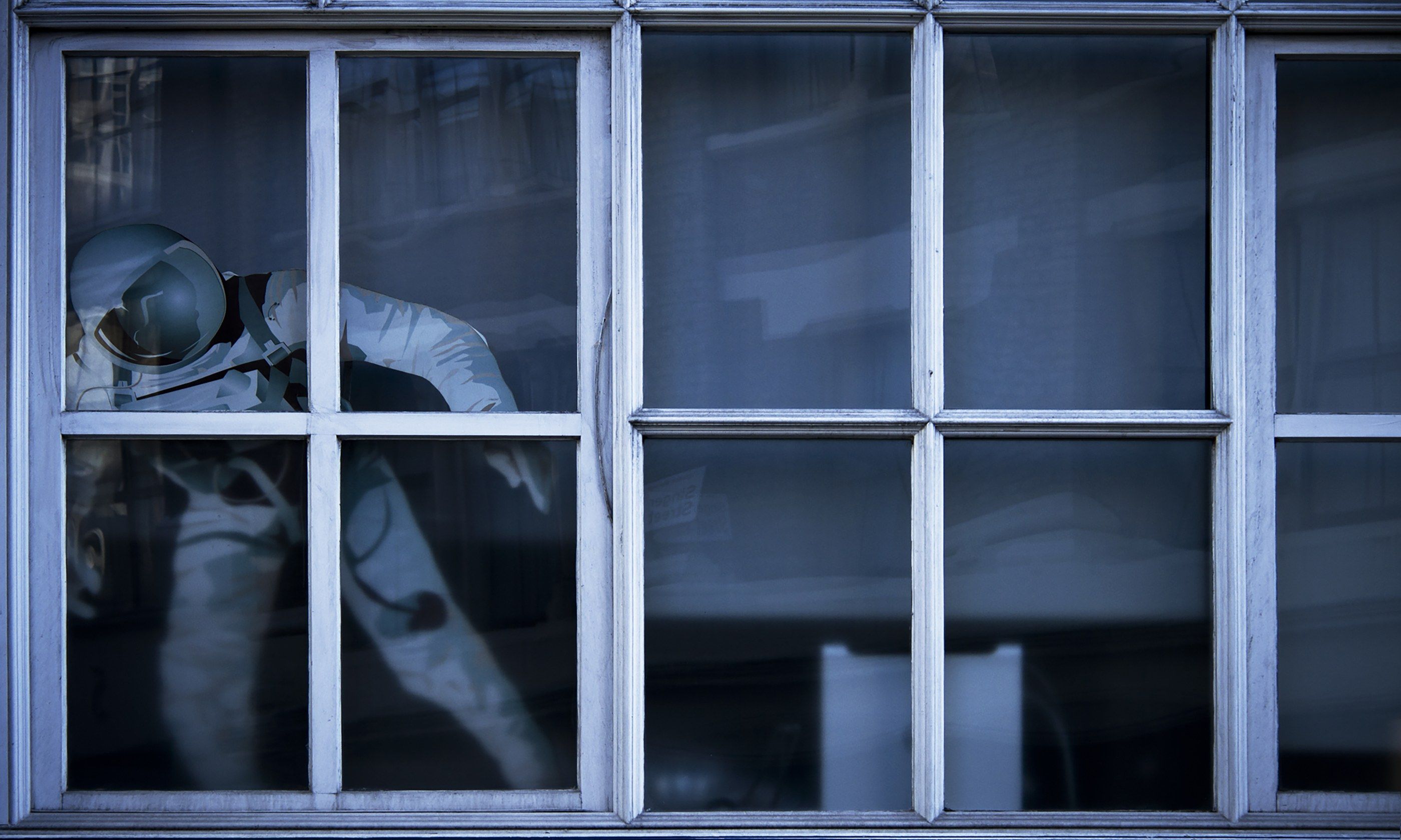 Figura de un astronauta detrás de una ventana de marco blanco, en tonos azules