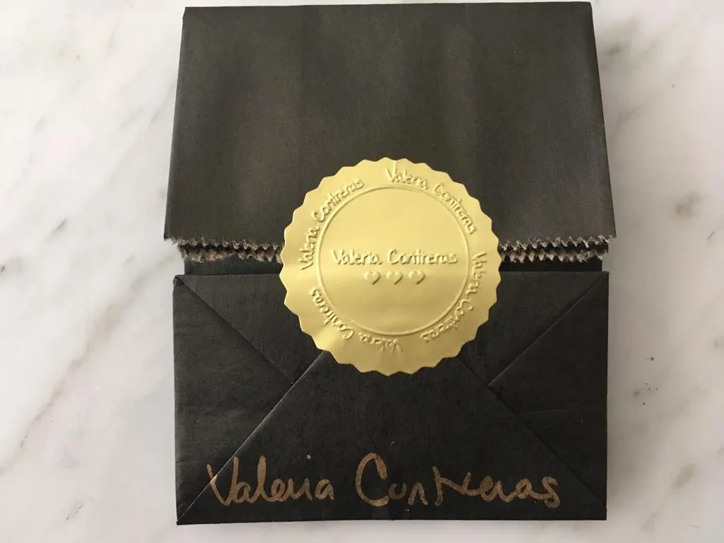 Bolsa negra de entrega cerrada con un sello dorado y la firma de Valeria en dorado