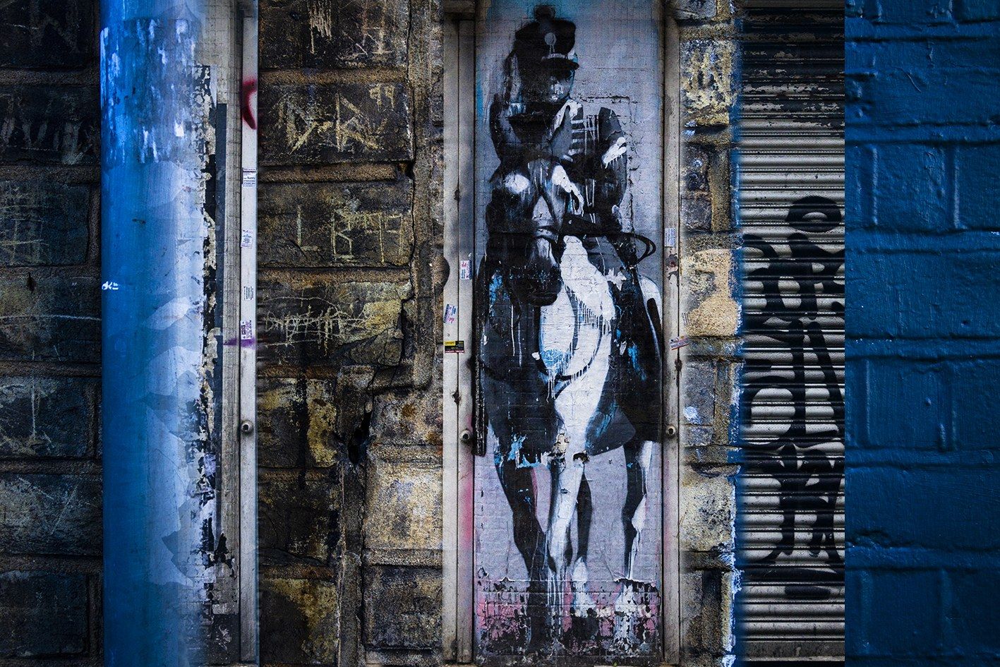 Stencil de un soldado a caballo sobre un muro desgastado, entre tuberías y cortinas metálicas azules