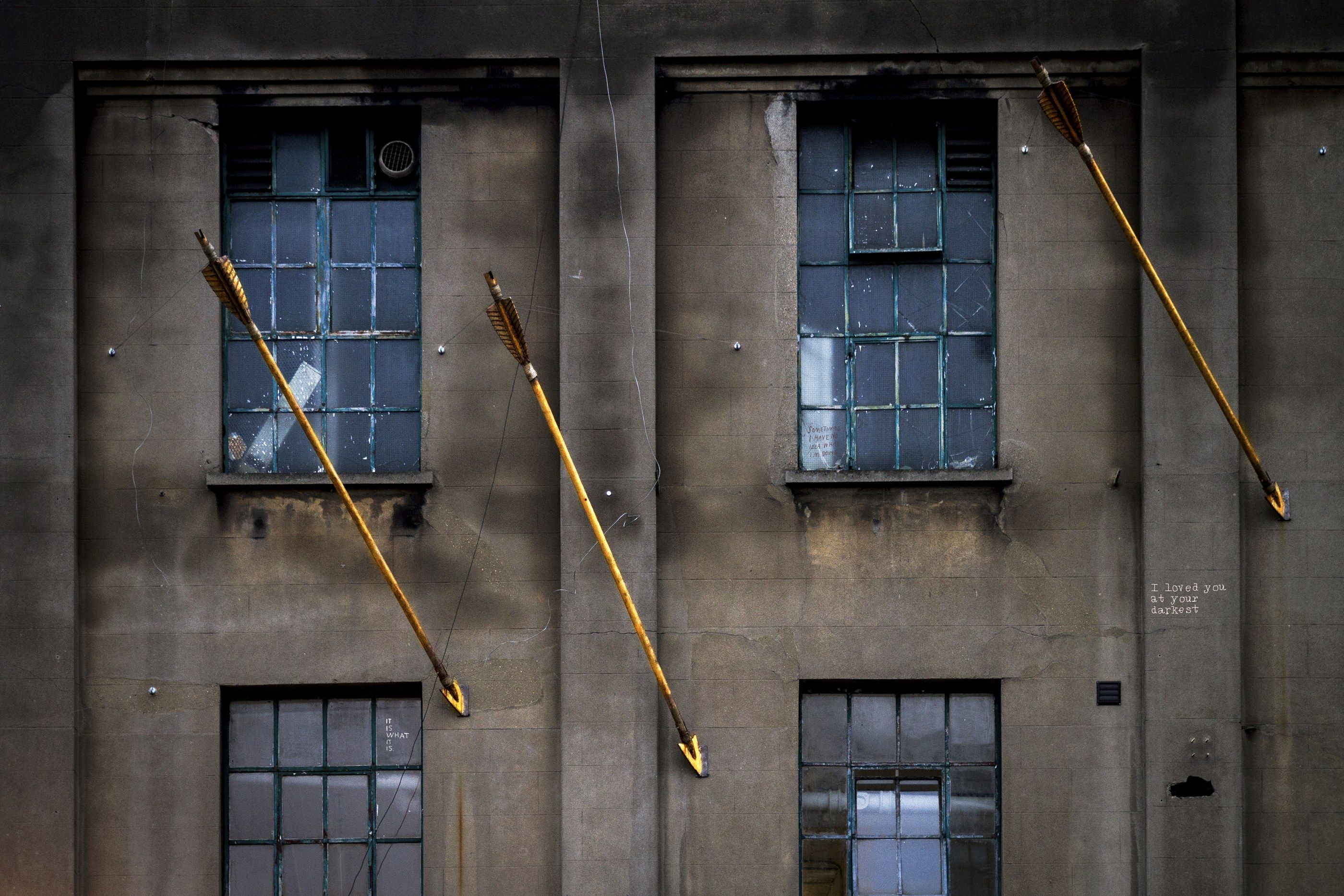 Fachada gris de un edificio antiguo con ventanas y tres flechas doradas incrustadas en diagonal